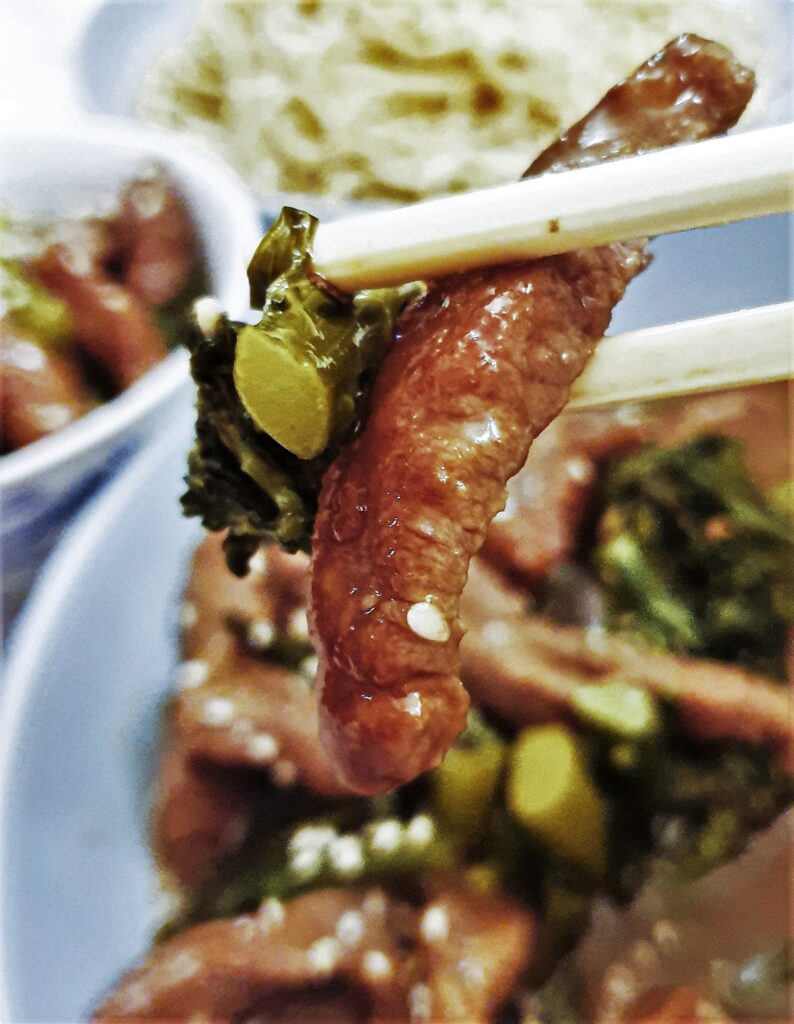 A piece of beef with brocoli held in chopsticks.