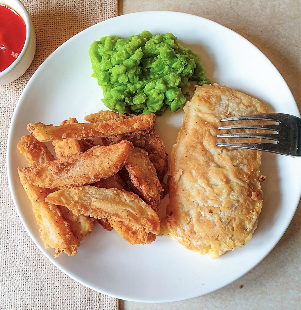 A plate of fish and crispy French fries with mushy peas.