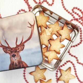 Shortbread stars in a tin with a picture of a stag's head, next to a strand of red beads for decoration.