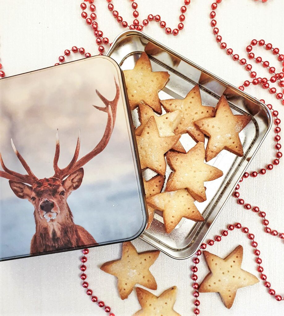 Shortbread stars in a tin with a picture of a stag's head, next to a strand of red beads for decoration.