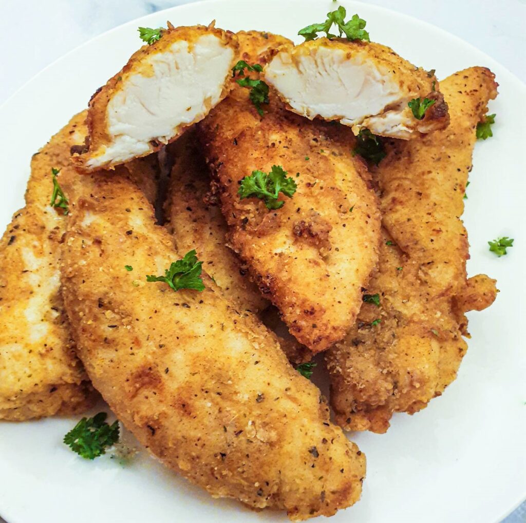 A pile of fried chicken tenderloins, with one cut in half to show the texture of the fried chicken.