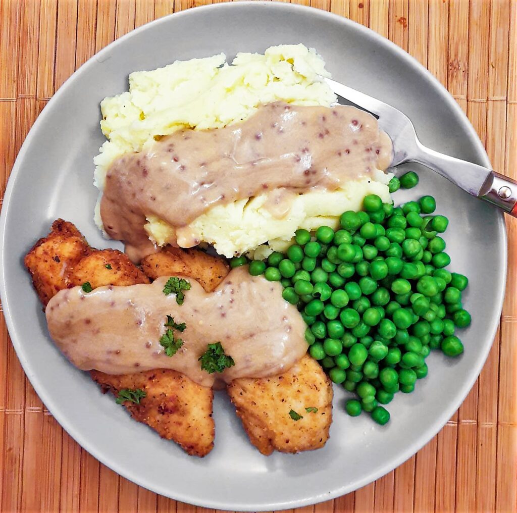 Overhead shot of a plate of fried chicken, mashed potatoes and peas.