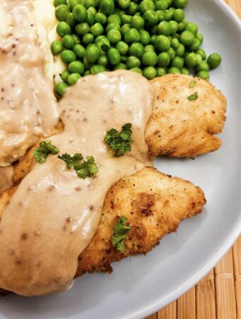 Fried chicken tenderloins on a plate with mashed potatoes and peas, covered with creamy mustard gravy.