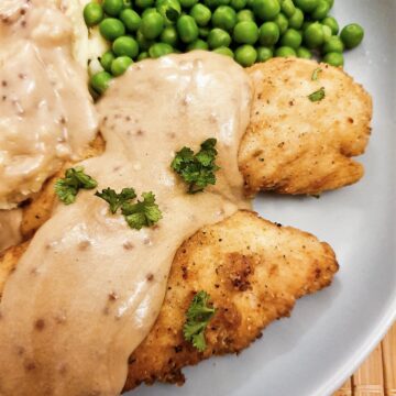 Fried chicken tenderloins on a plate with mashed potatoes and peas, covered with creamy mustard gravy.