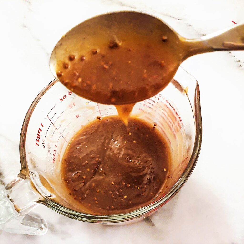 A spoonful of gravy being lifted from a jug, showing the consistency before the cream is added.