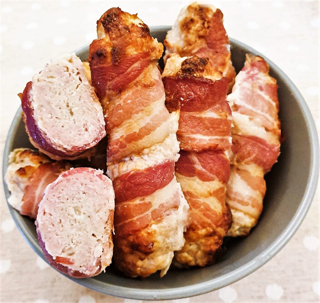 Closeup of pigs in blankets, with one cut open to show the texture of the sausage.