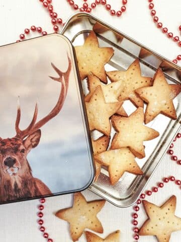 Shortbread stars in a tin with a picture of a stag's head, next to a strand of red beads for decoration.