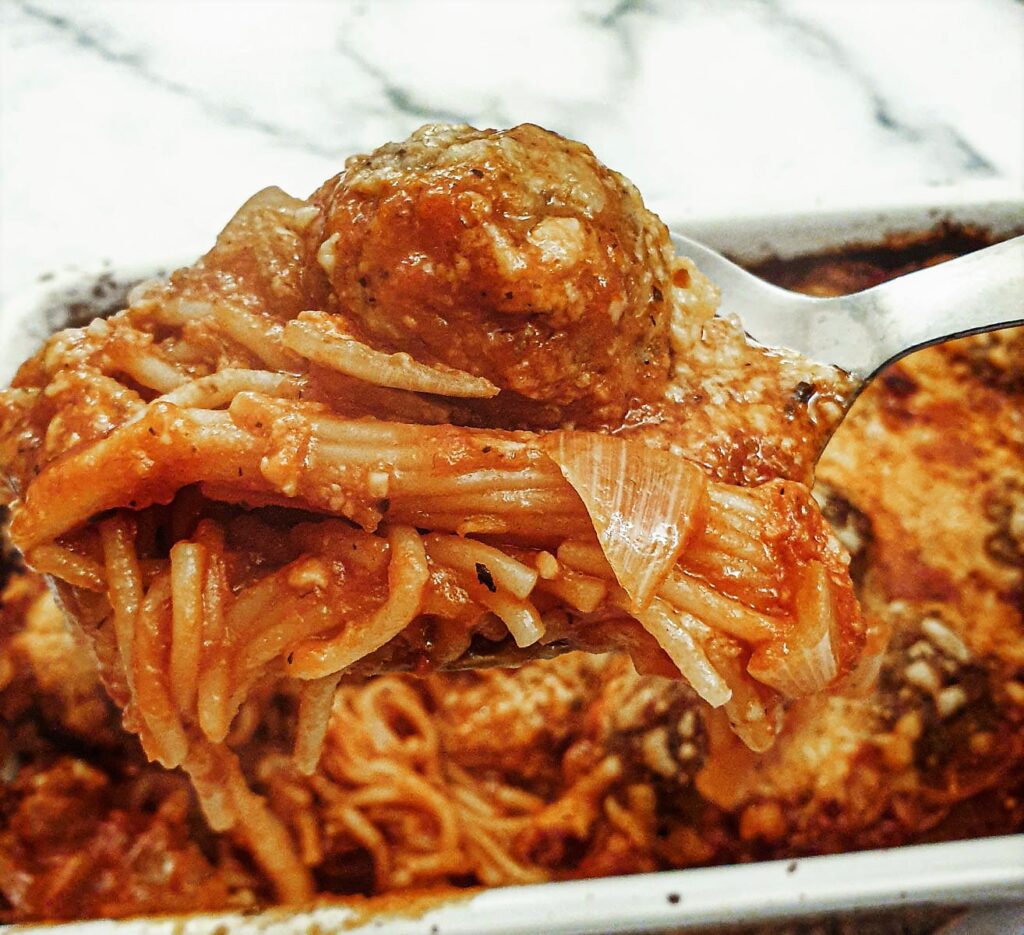 A spoonful of spaghetti and meatballs being lifted from the baking dish.