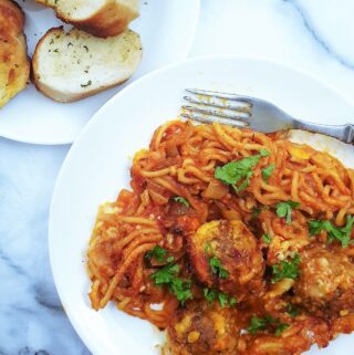 Oven baked spaghetti and meatballs on a plate next to a side dish of garlic bread slices.