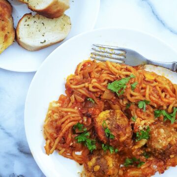 Oven baked spaghetti and meatballs on a plate next to a side dish of garlic bread slices.