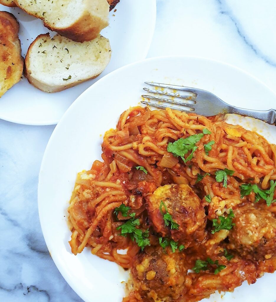 Oven baked spaghetti and meatballs on a plate next to a  side dish of garlic bread slices.