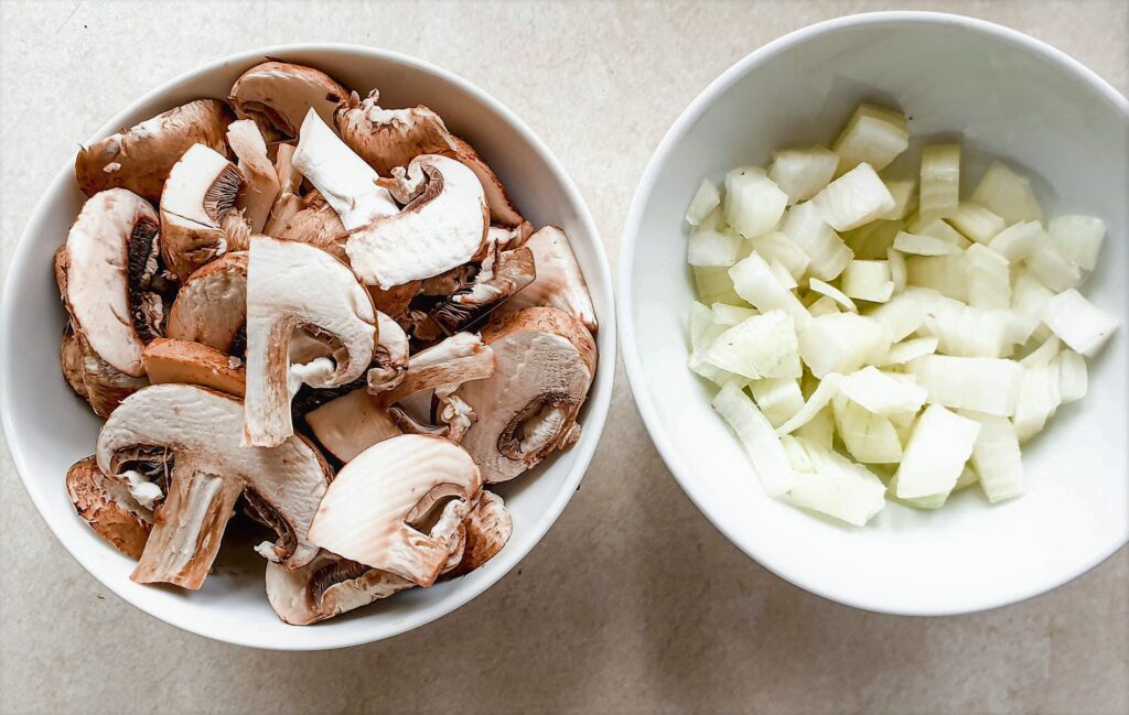 Two dishes, one containing  chopped mushrooms and the other contining chopped onions