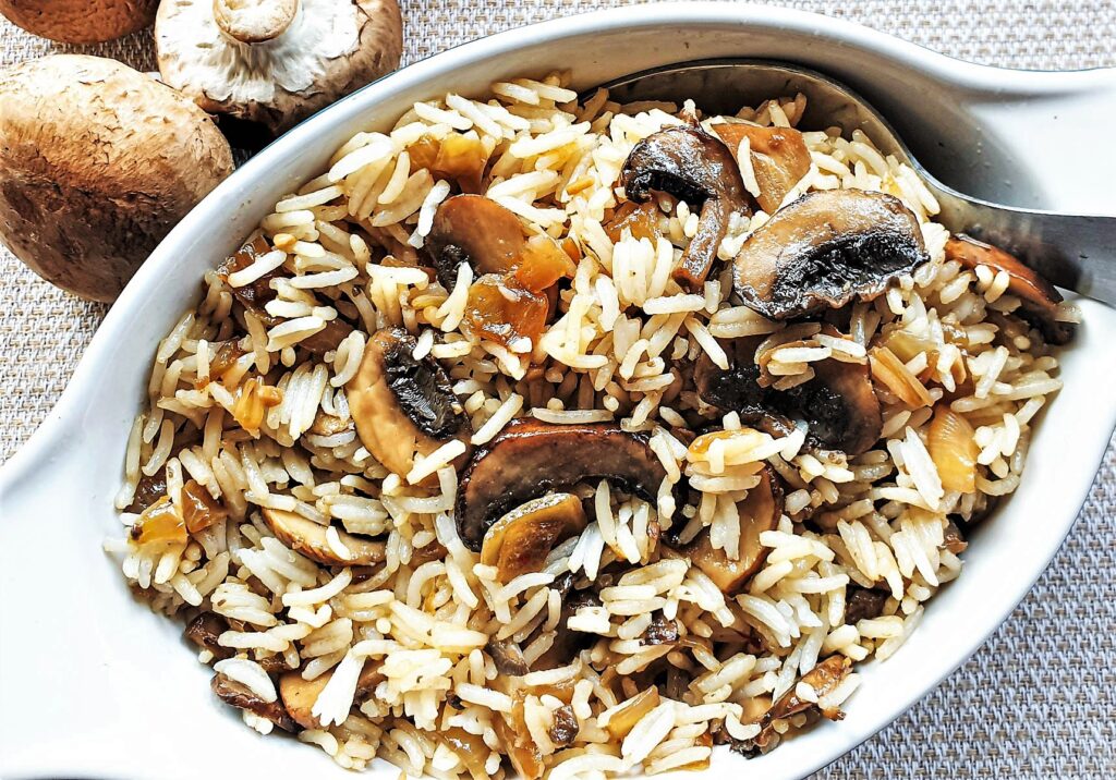 A dish of spicy mushroom fried rice next to raw mushrooms.