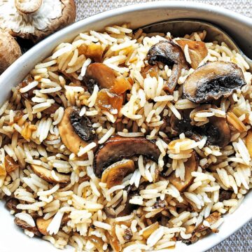 A dish of spicy mushroom fried rice next to raw mushrooms.