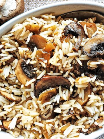 A dish of spicy mushroom fried rice next to raw mushrooms.