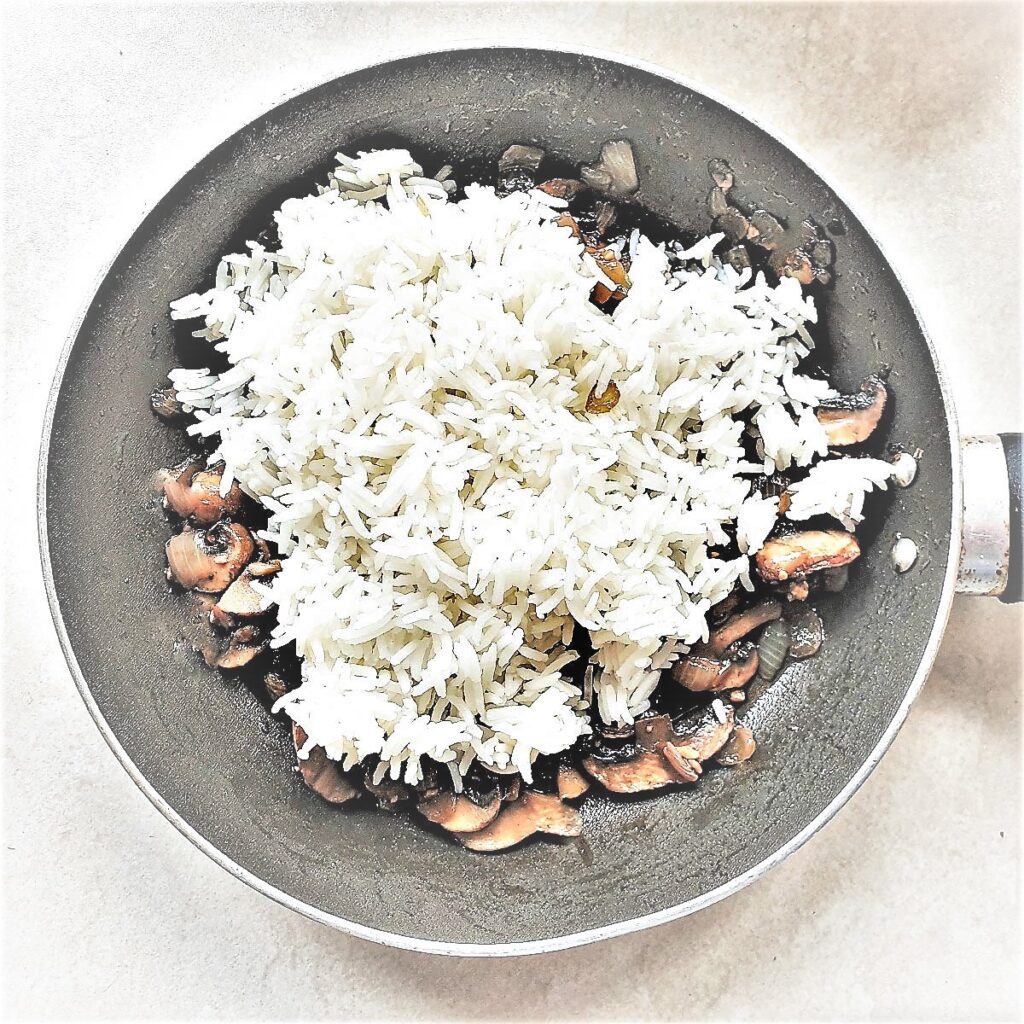 Rice being added to fried mushrooms and onions.