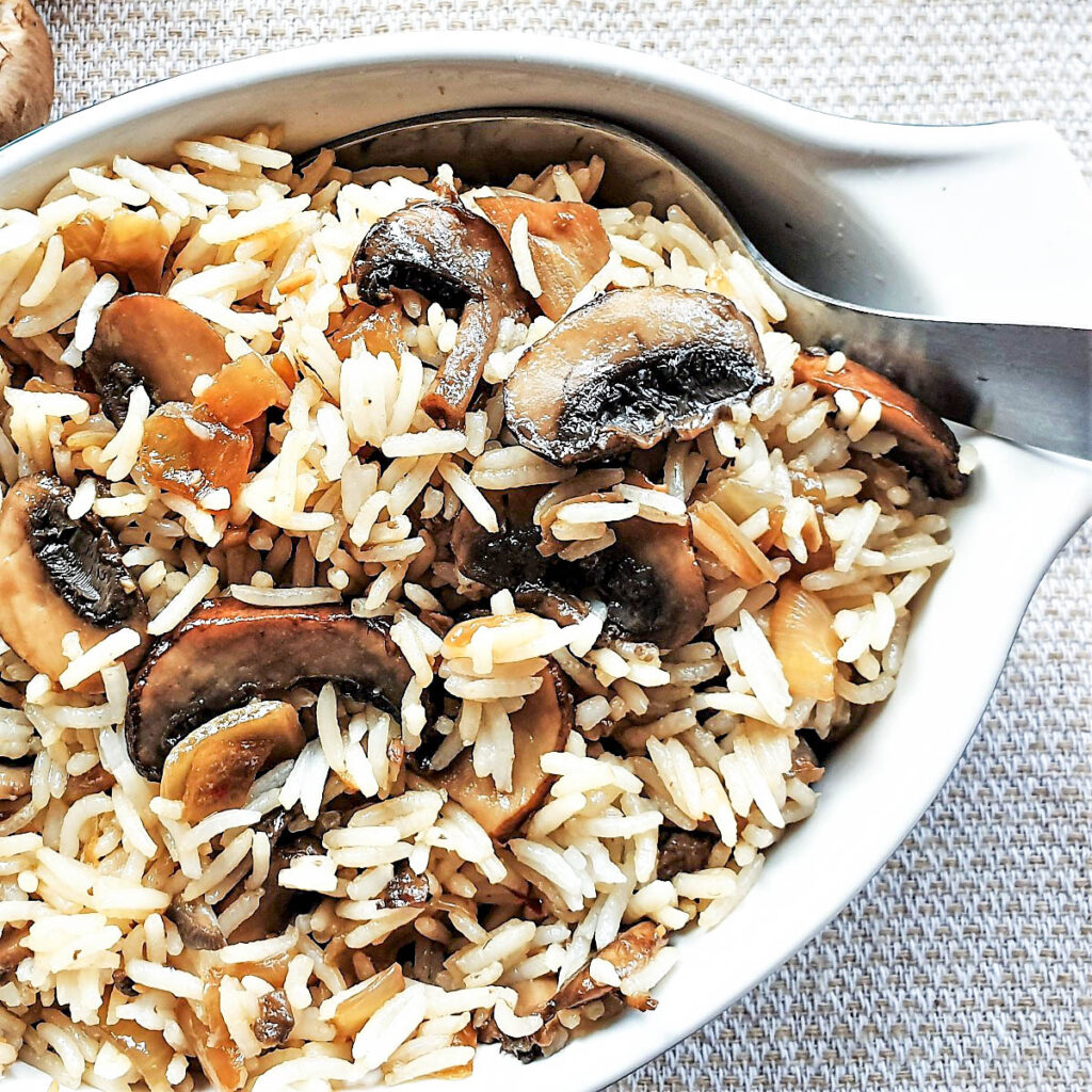 Close up of spicy mushroom fried rice in a serving dish with a spoon.