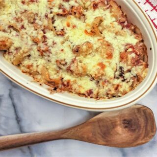 A baking dish filled with cheesy bully beef pasta casserole next to a large wooden spoon.