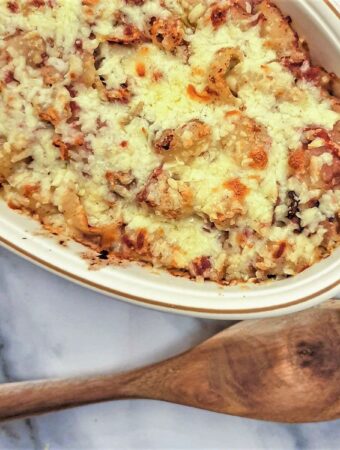 A baking dish filled with cheesy bully beef pasta casserole next to a large wooden spoon.