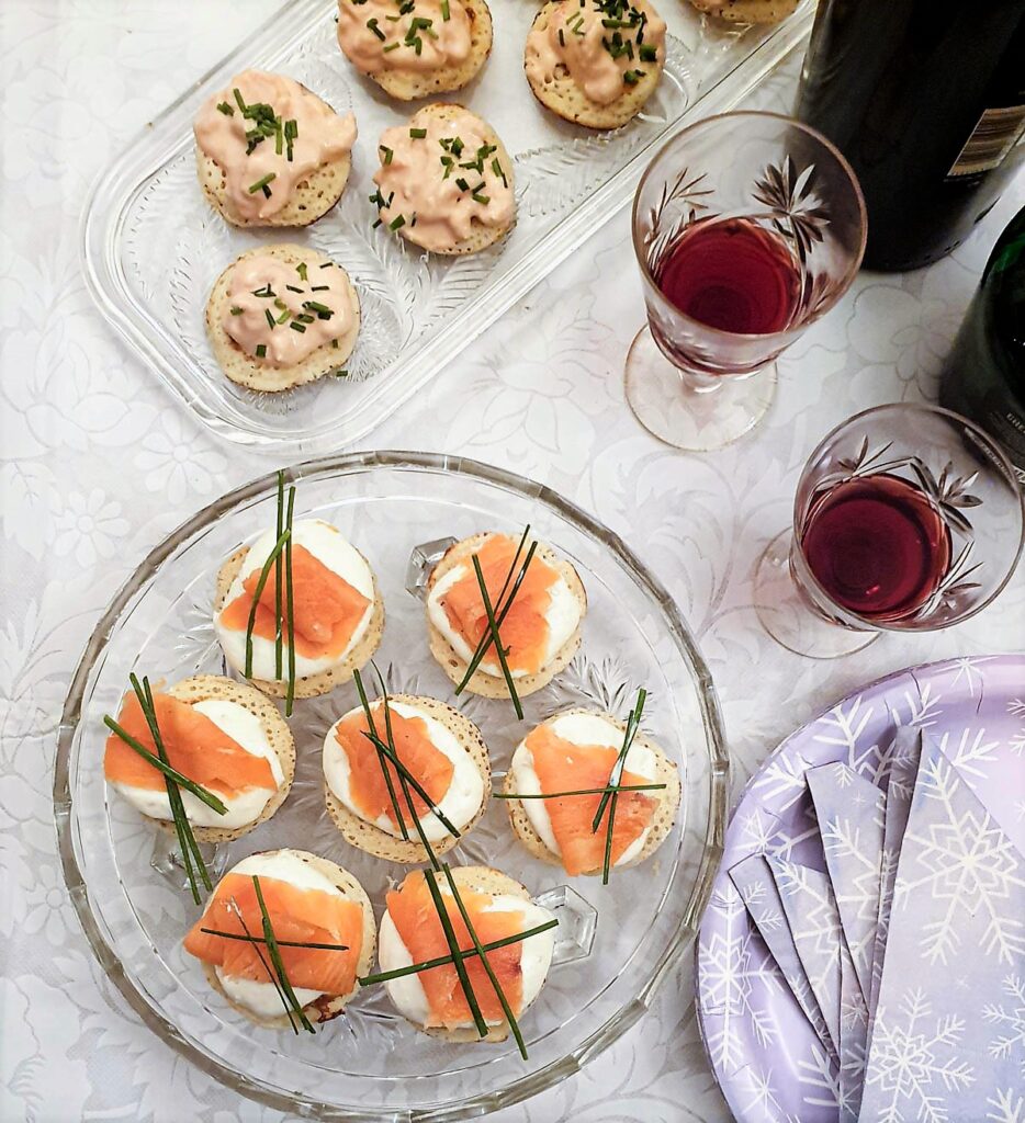 A selection of blinis on glass platters next to glasses of wine.