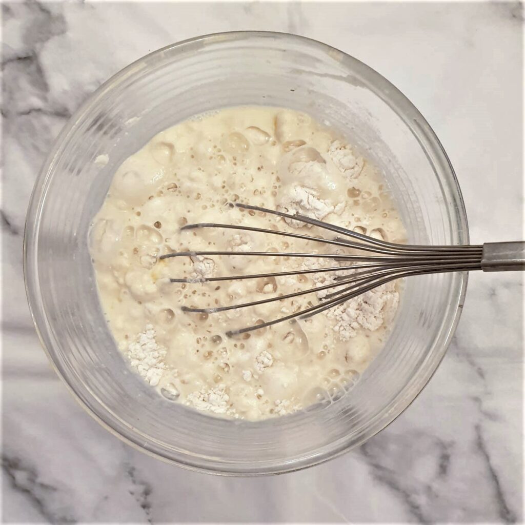 Blini batter being mixed in a bowl with a balloon whisk.