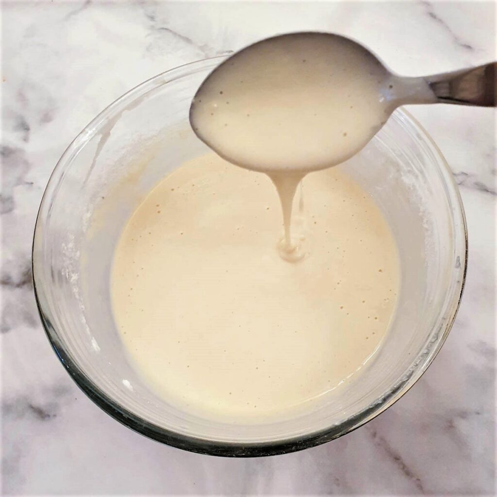 Blini batter being dropped from a spoon to show the consistency.