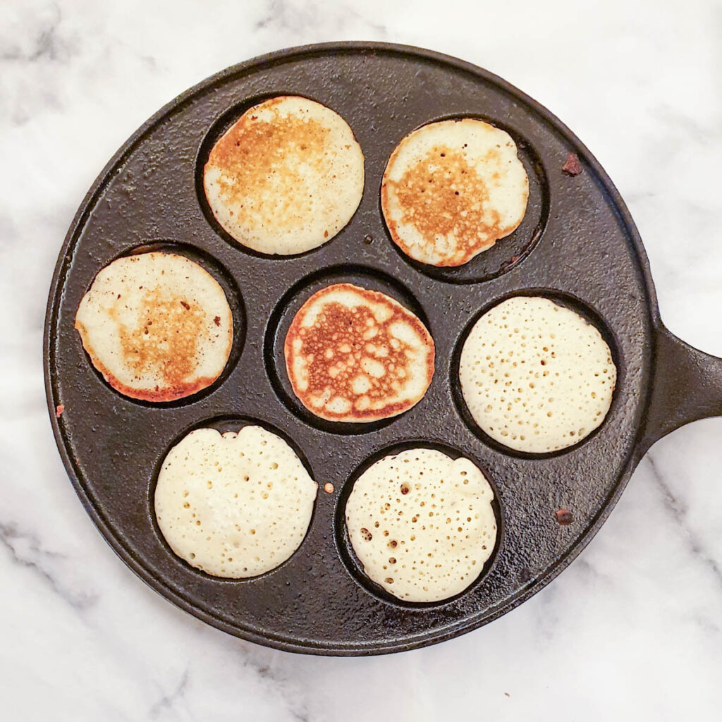 Blinis being browned in a blini pan.