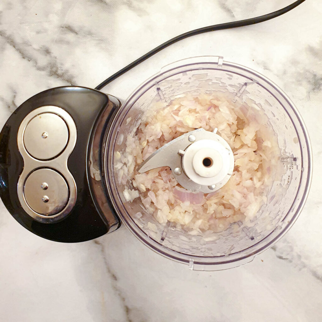 Onions and pineapple being pulsed in a food processor.