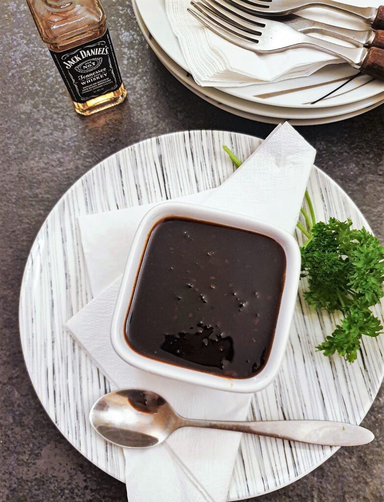 An individual bowl of Jack Daniels dipping sauce on a plate with a spoon.