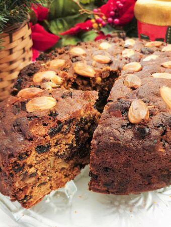 A christmas cake on a glass plate with a slice cut and offset to show the inside of the cake.