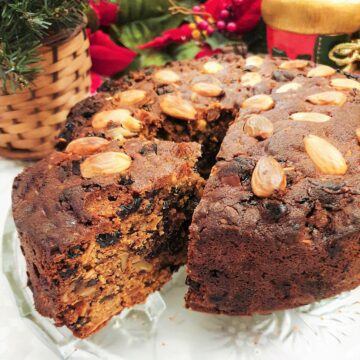 A christmas cake on a glass plate with a slice cut and offset to show the inside of the cake.