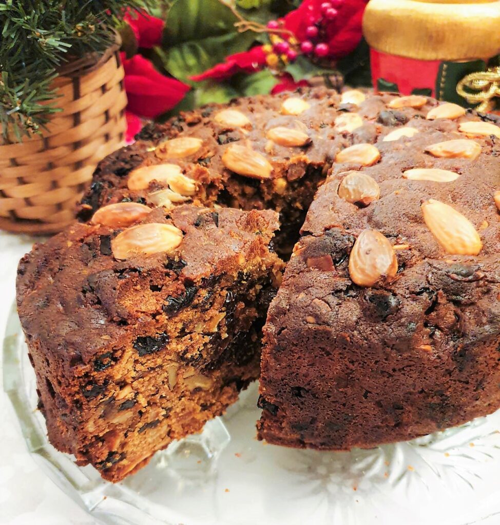 A christmas cake on a glass plate with a slice cut and offset to show the inside of the cake.