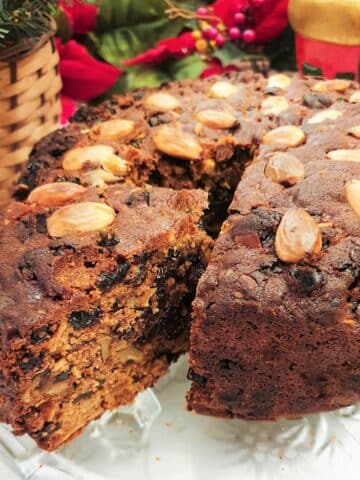 A christmas cake on a glass plate with a slice cut and offset to show the inside of the cake.