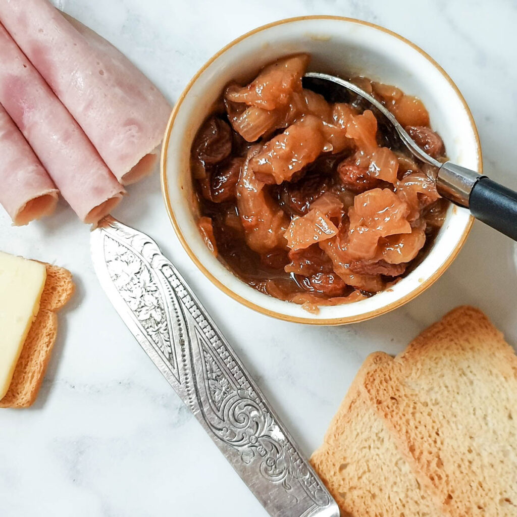 Overhead shot of pear and onion chutney in a dish next to slices of rolled ham.