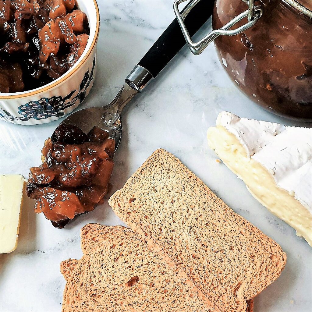 A spoonful of chutney on a platter with cheese and crackers.