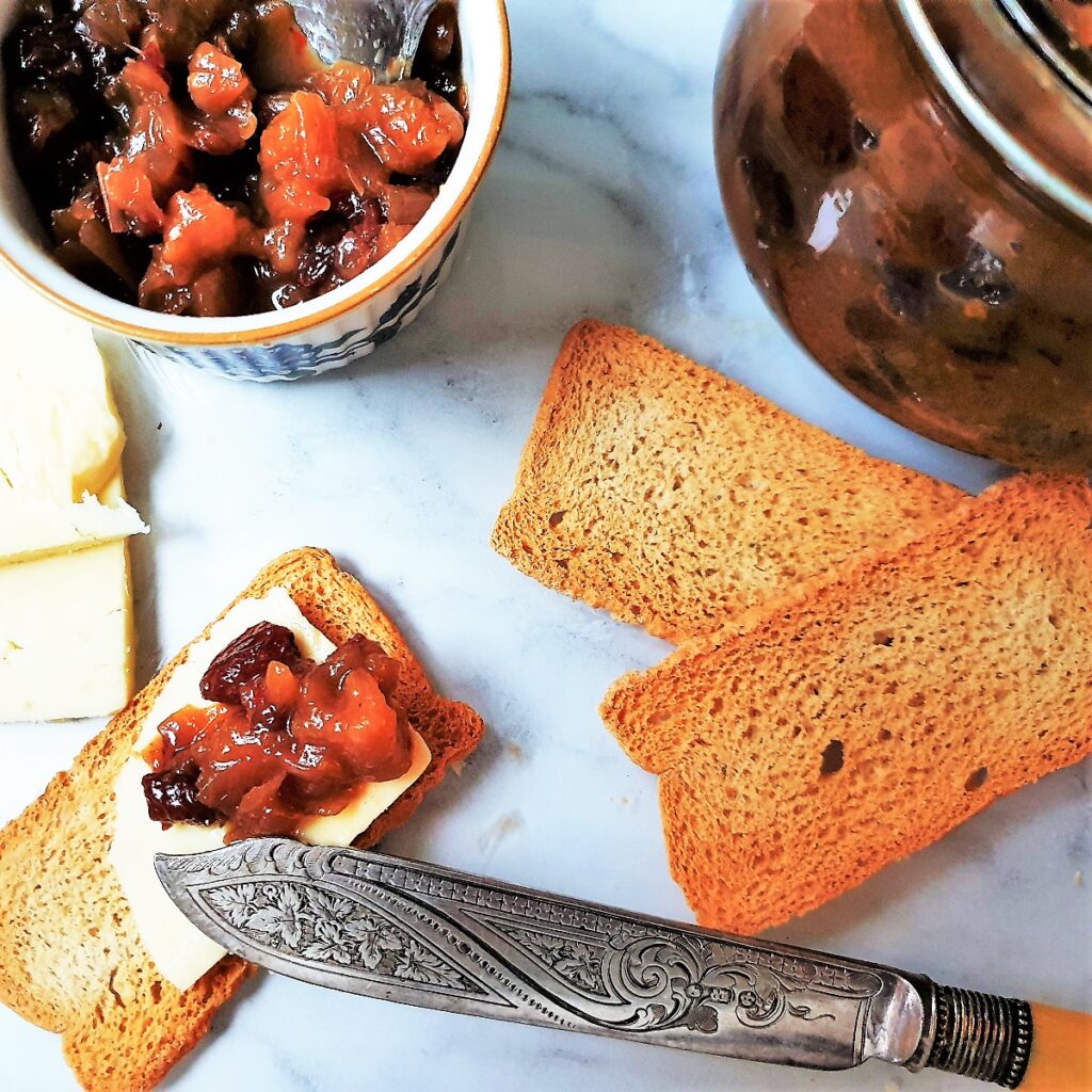 Pear and onion chutney being spread onto a slice of cheese on a cracker.