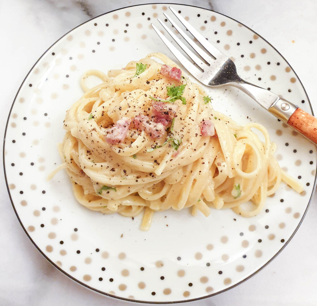 A helping of creamy spaghetti carbonara on a plate with a fork.