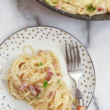 A plate of spaghetti carbonara sprinkled with black pepper.