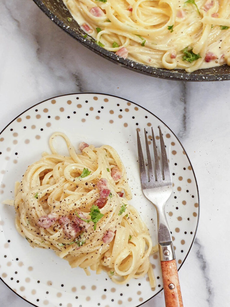 A plate of spaghetti carbonara sprinkled with black pepper.