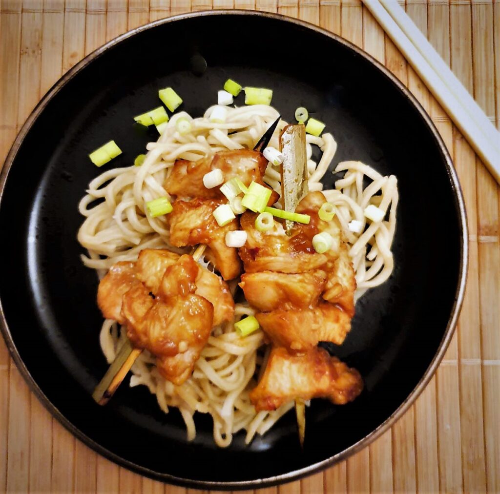 Two chicken skewers on a bed of noodles.