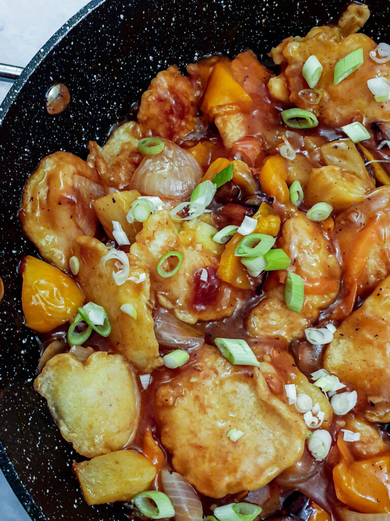 Pieces of chicken coated in batter, covered in sauce and garnished with spring onions.