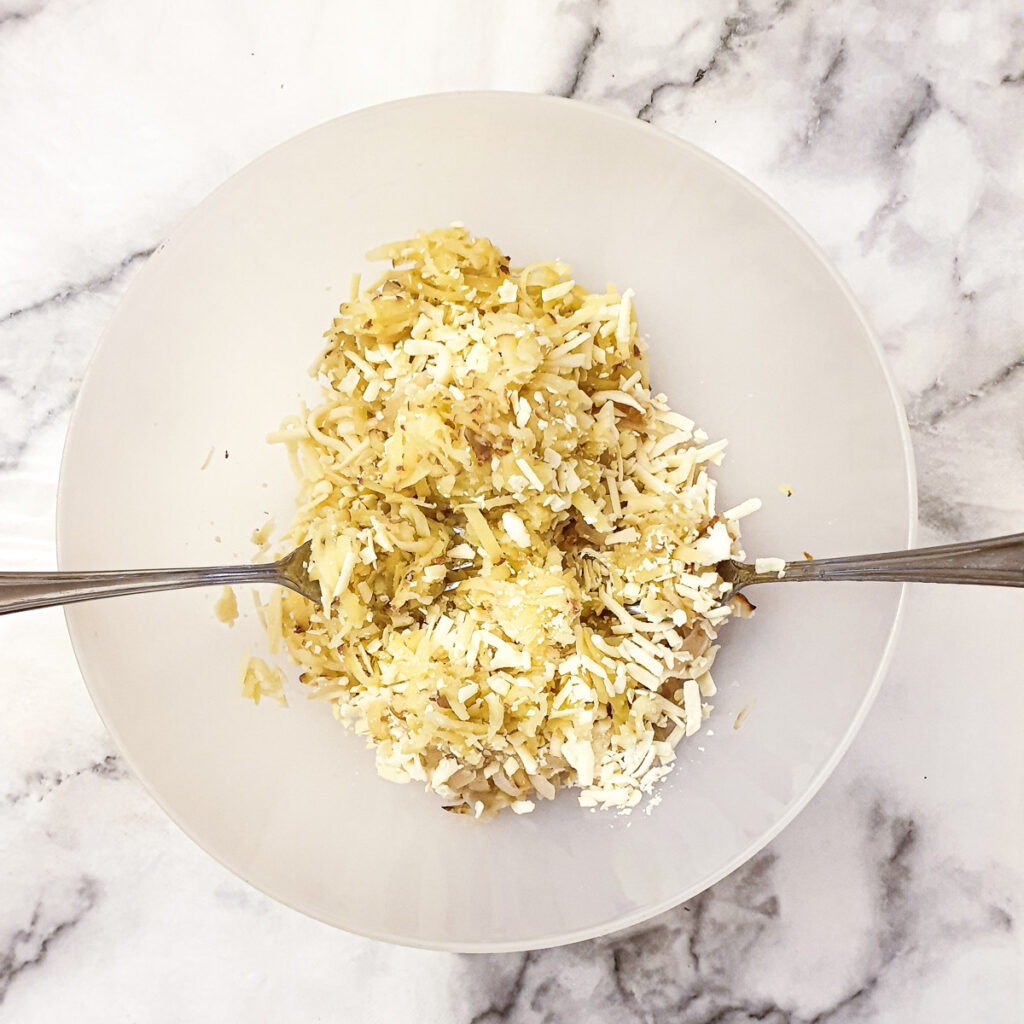 A bowl of combined ingredients being mixed with two forks.