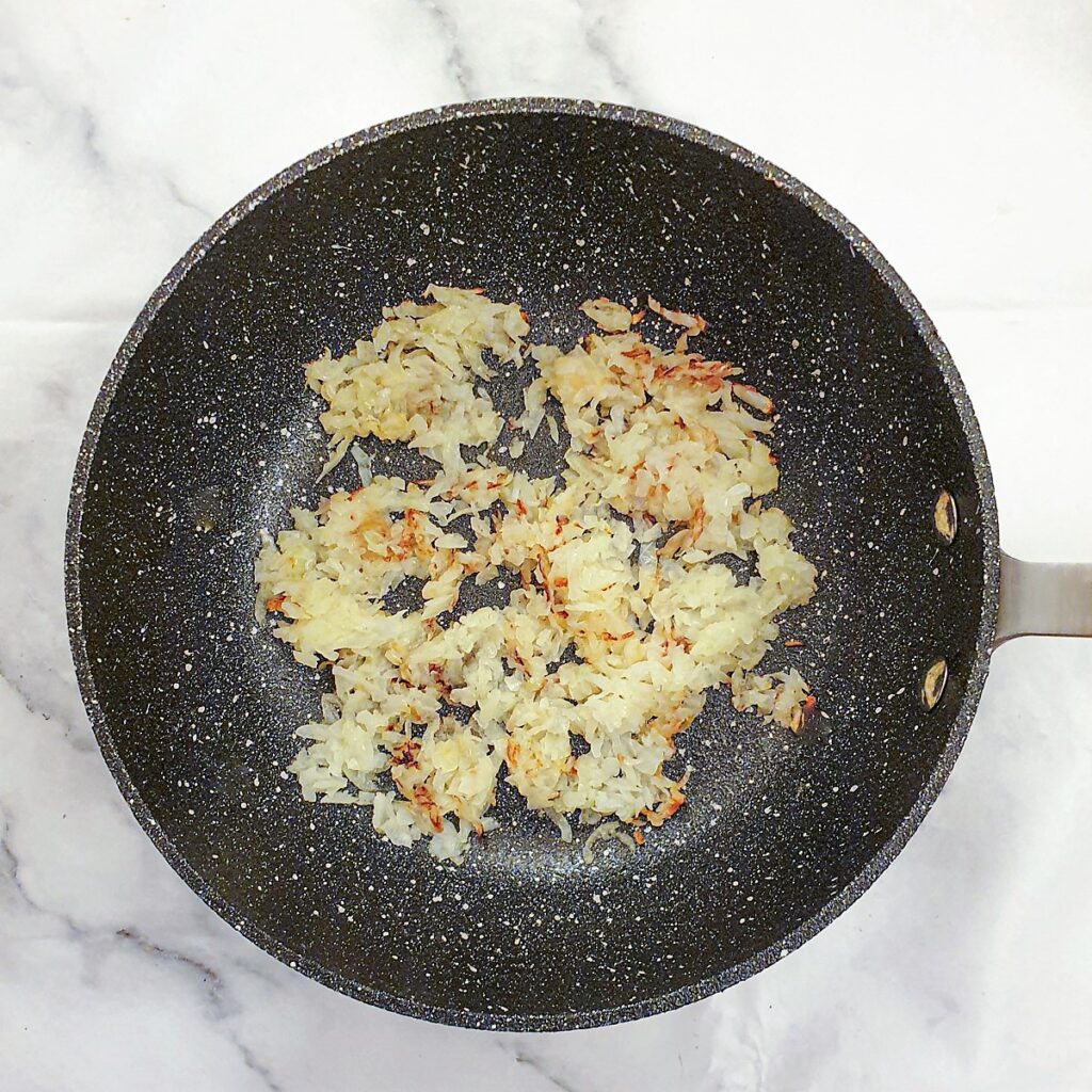 Grated onions being browned in a frying pan.