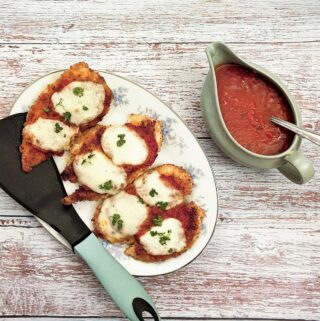 Servings of chicken parmigiana on a plate, next to a dish of marinara sauce.