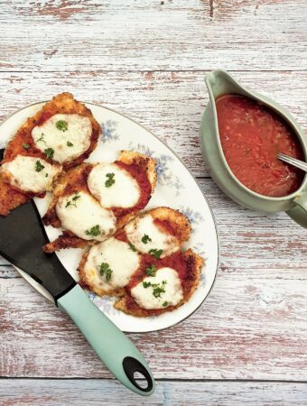 Servings of chicken parmigiana on a plate, next to a dish of marinara sauce.