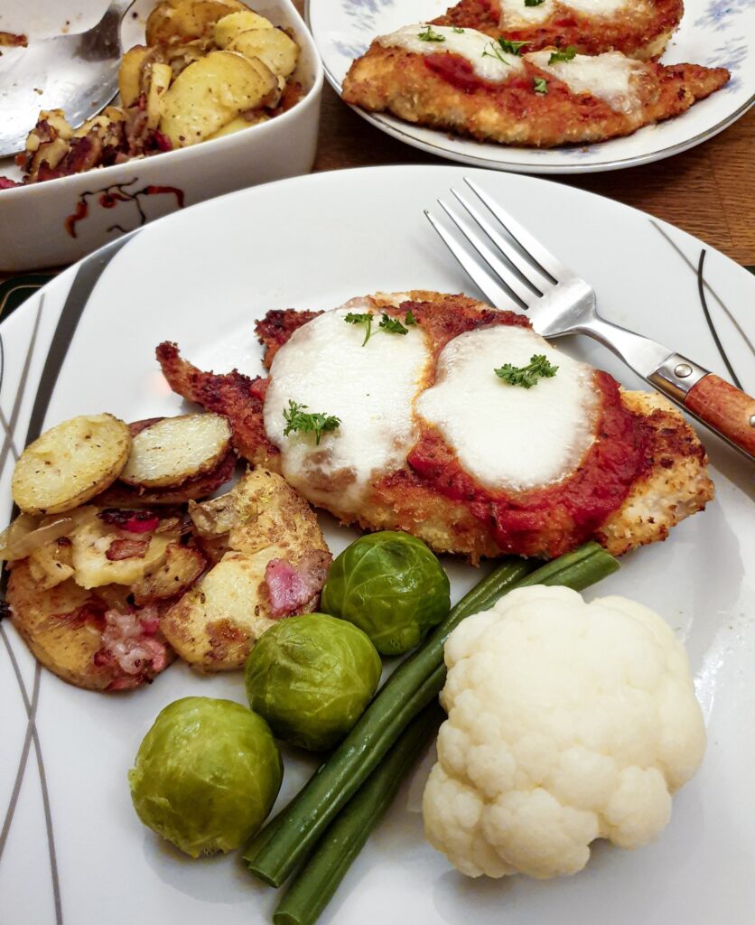 Chicken parmesan on a plate with vegetables.