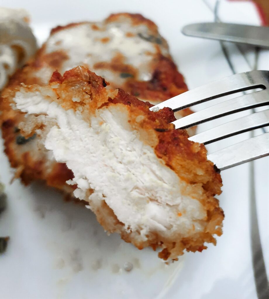 A slice of chicken on a fork, showing the texture of the chicken and the crispy breadcrumbs surrounding it.