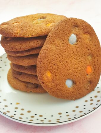 A pile of giant Smartie cookies on a plate with one cookie standing on its side.