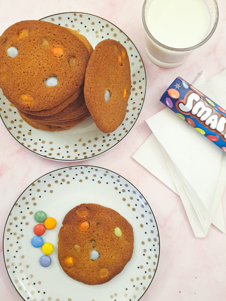 Over head shot of a pile of Smartie cookies with a glass of milk and a tube of Smarties.