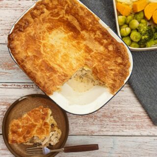 An overhead shot of granny's chicken pie with a slice removed and served on a plate next to the baking dish.